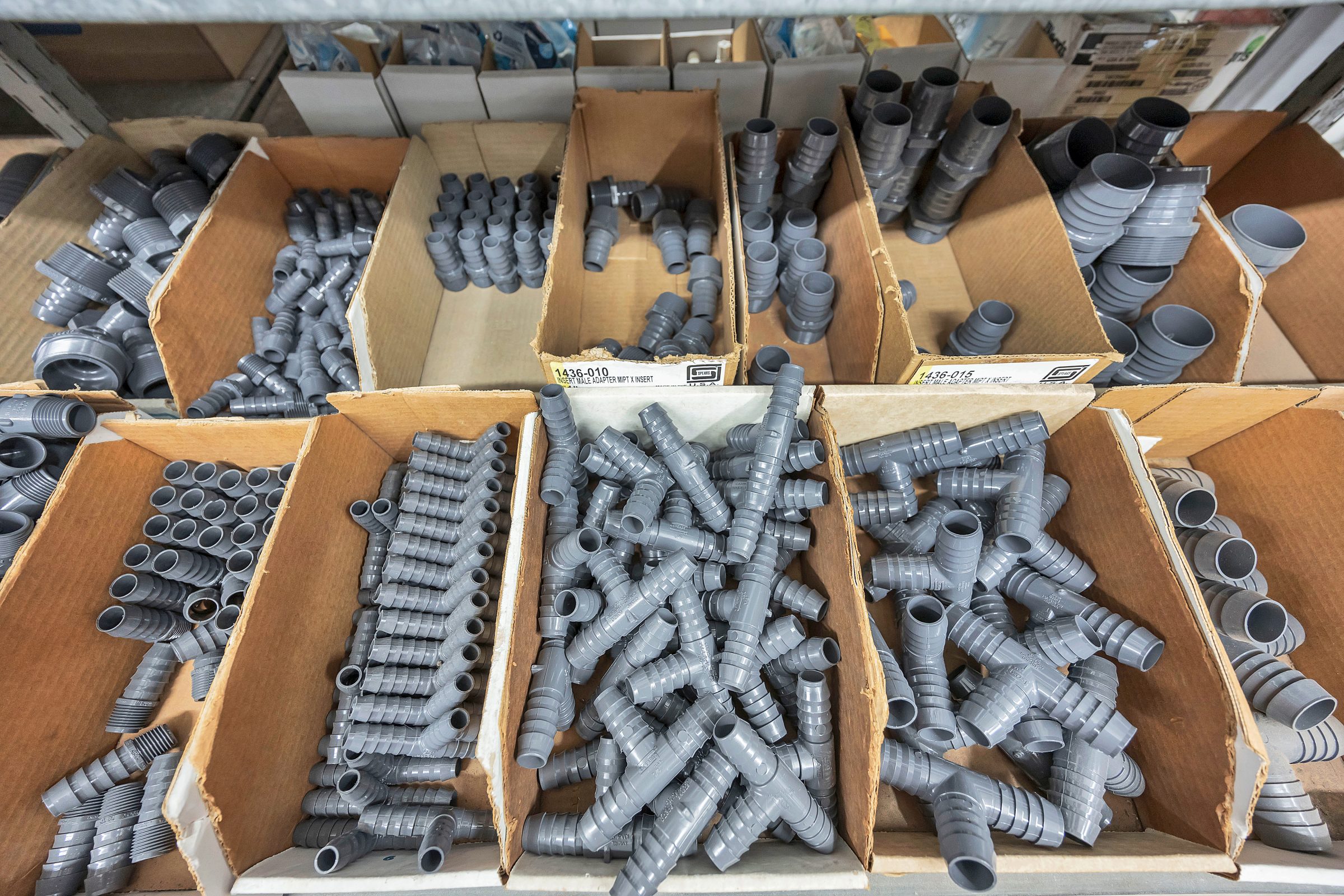 Plastic pipe fittings in cardboard boxes on shelves.