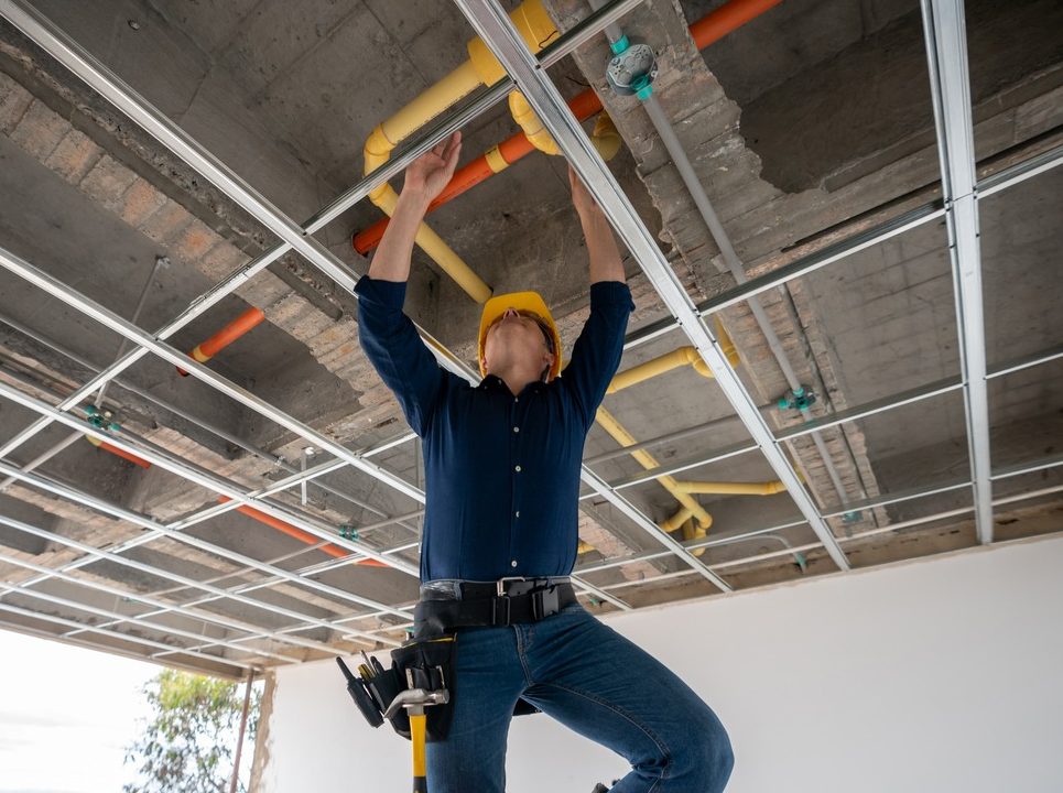 Worker installing ceiling pipes on stepladder